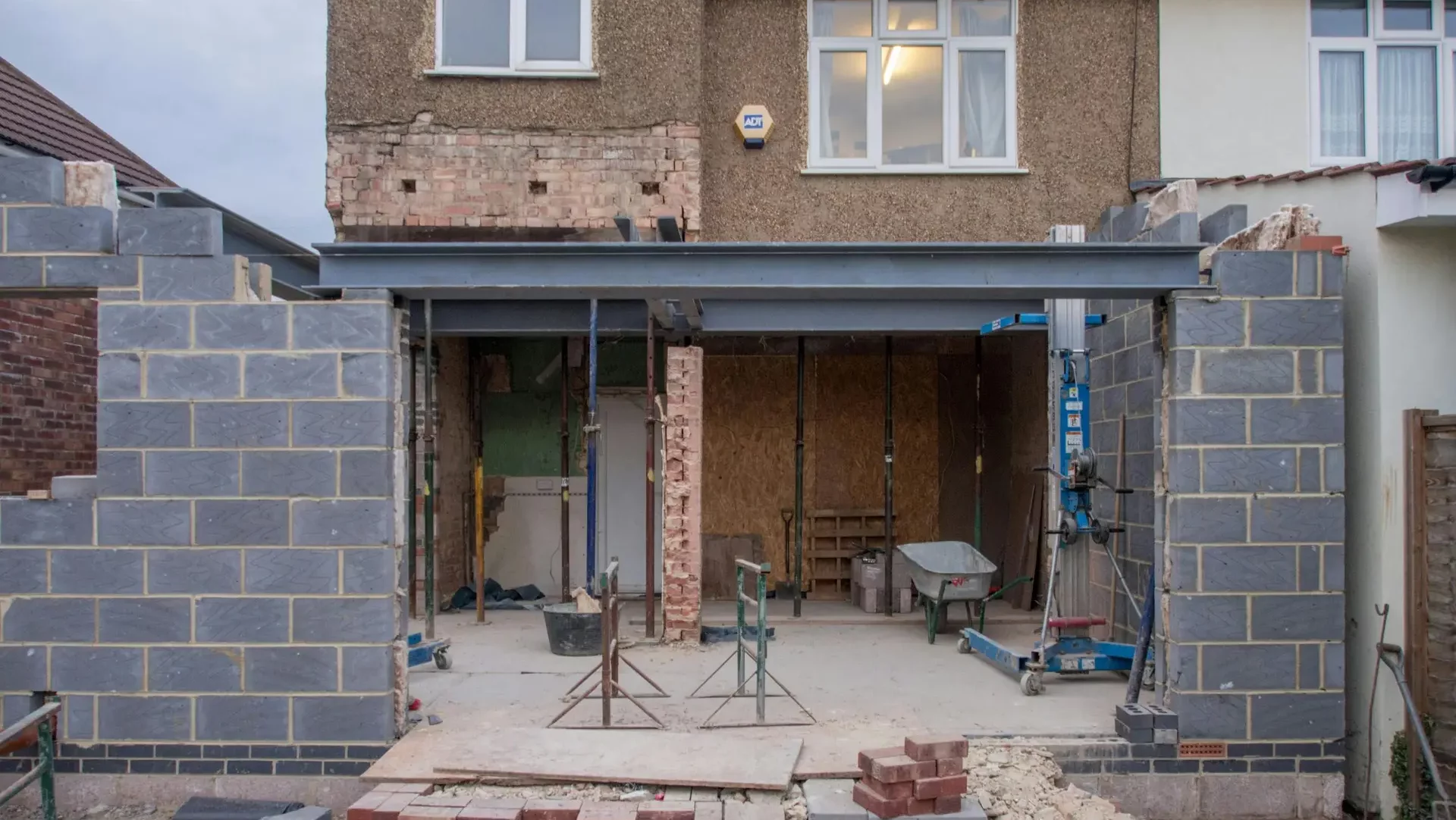 Brick house under renovation with an extension in progress. Visible construction site materials and structure.