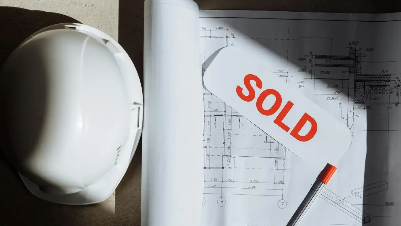 Blueprints with a sold sign and hard hat on a sunlit surface, symbolizing real estate success.