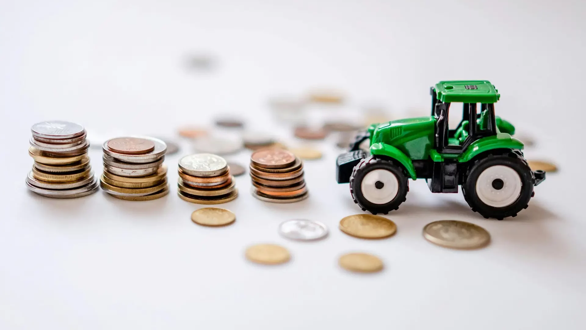 A miniature green tractor beside stacks of coins in a creative still life scene.